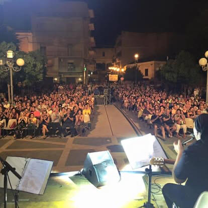 UntitledPeppone e Universo De Andrè Una fotografia del concerto 'Universo De André' tenutosi a Zafferana. Peppone con i musicisti di De André è schierato sul palco mentre ringrazia il folto pubblico che applaude dalle gradinate dell'arena. Al centro, uno dei musicisti tiene un tamburello sol